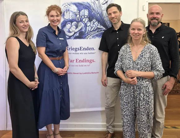 Gruppenfoto von fünf Personen vor dem Banner der Ausstellung „KriegsEnden“. Die Aufnahme entstand in den Ausstellungsräumen.