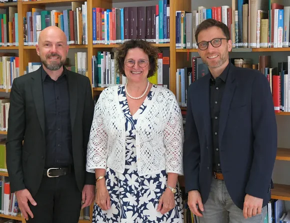 Zwei Männer und eine Frau stehen vor einem Bücherregal