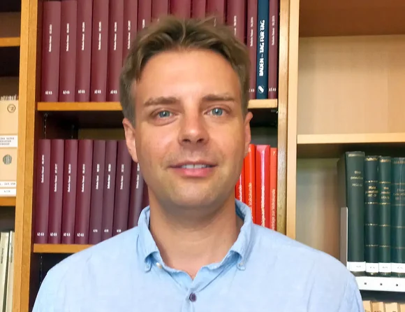 Ein junger Mann steht vor einem Bücherregal.