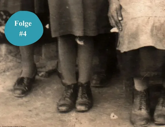 Ausschnitt aus einer historischen Fotografie mit einem Detail der Füße dreier Mädchen in dicken Strümpfen und schwarzen Schuhen.